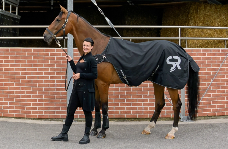 Ein Pferd und eine Reiterin stehen vor einer Führanlag und das Pferd hat die Führanlagendecke Cornwell auf