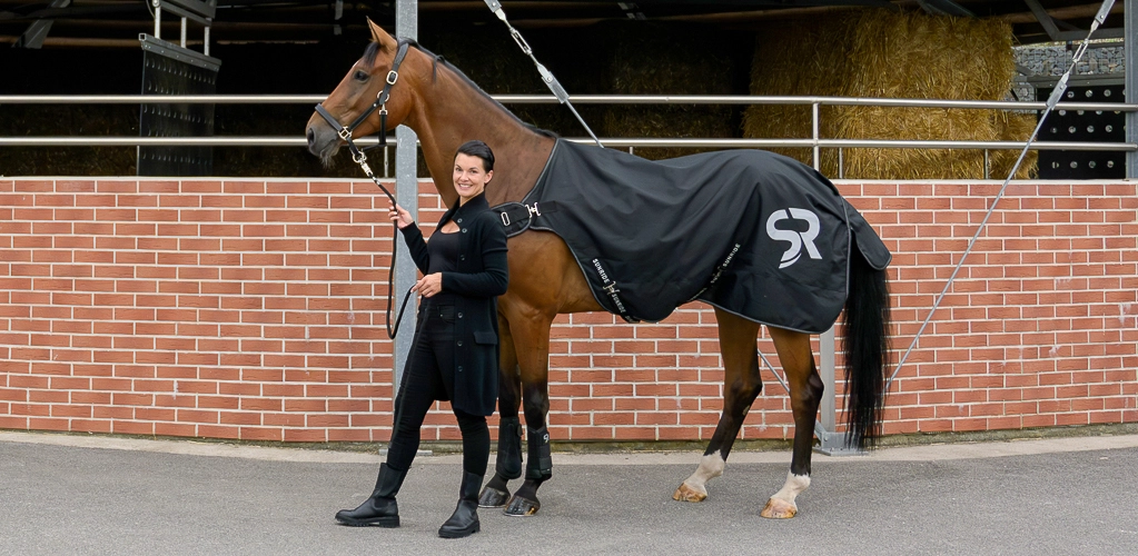 Ein Pferd und eine Reiterin stehen vor einer Führanlag und das Pferd hat die Führanlagendecke Cornwell auf