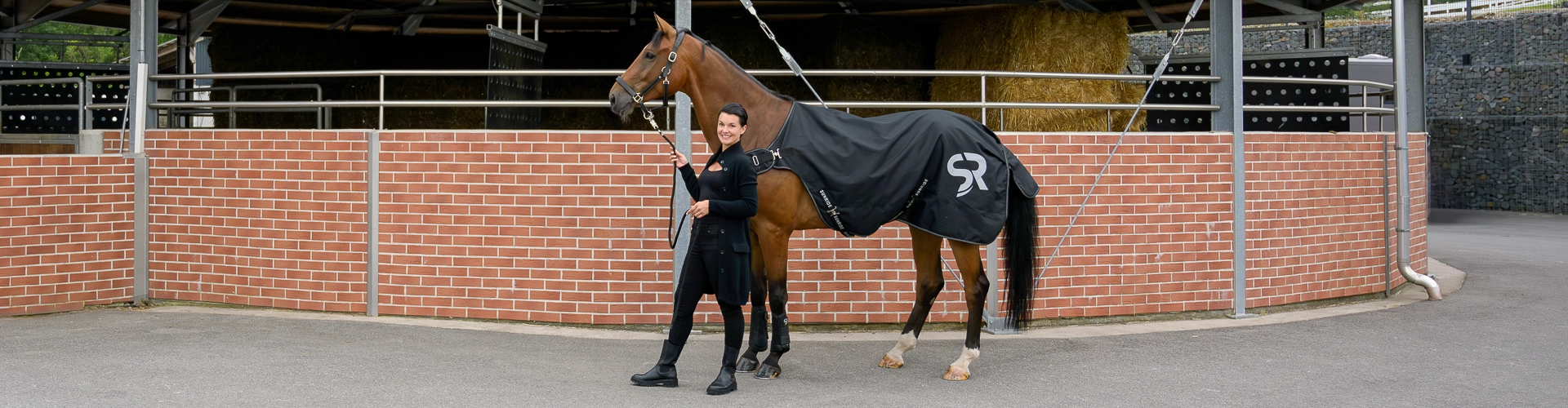 Ein Pferd und eine Reiterin stehen vor einer Führanlag und das Pferd hat die Führanlagendecke Cornwell auf