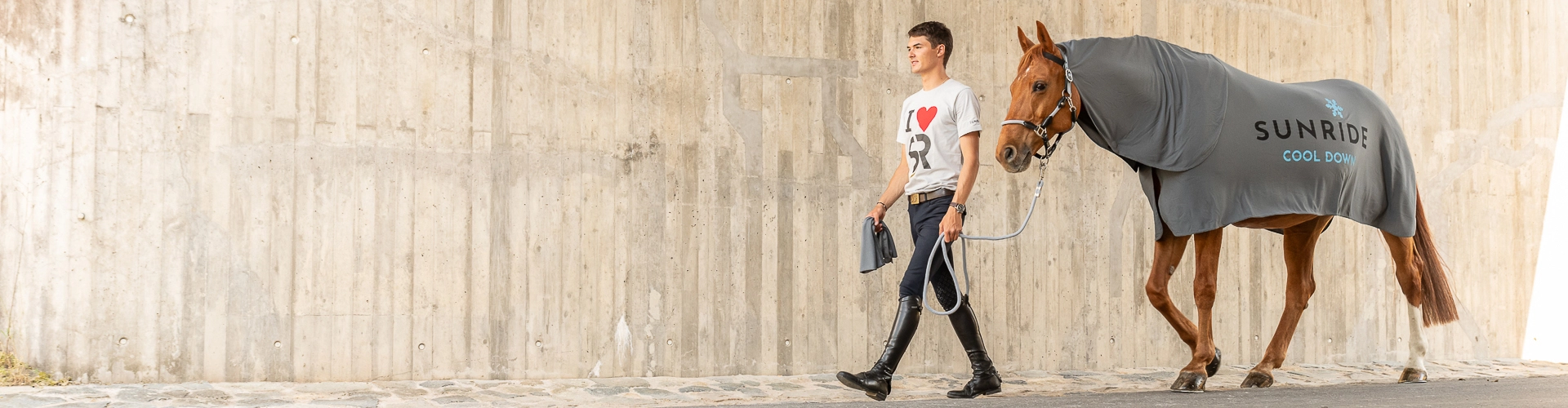 Ein Pferd wird an einer Betonmauer entlang geführt es das Pferd trägt die Kühldecke Cool Down